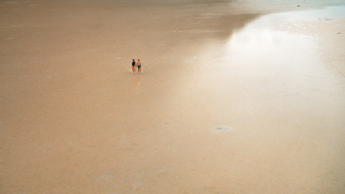 a couple of people standing on top of a sandy beach