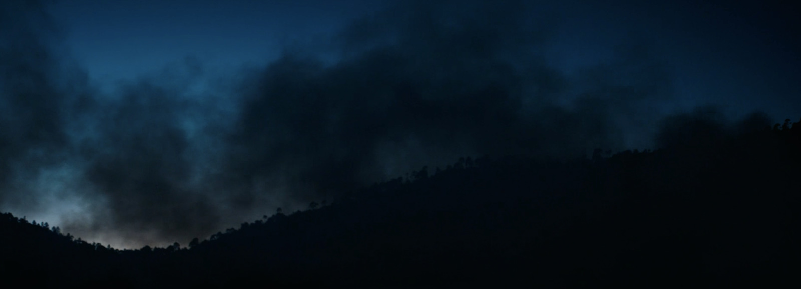 a dark sky with clouds and trees in the foreground