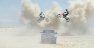 a car and two motorcyclists flying over a car in the desert