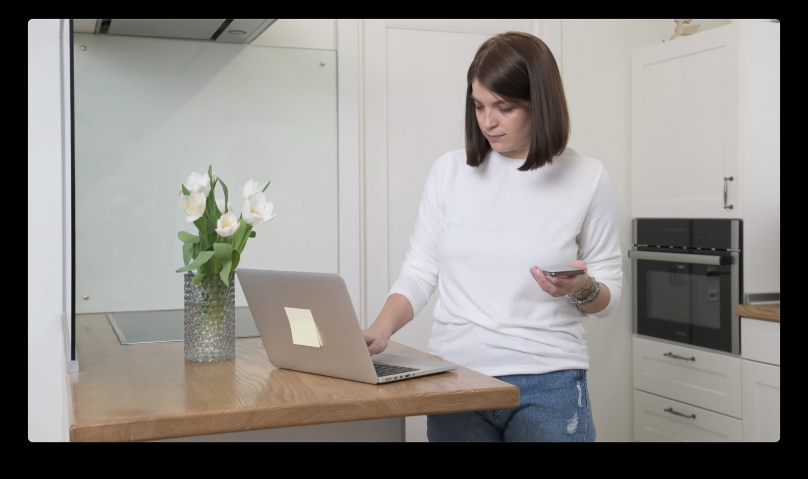 a woman holding a cell phone and looking at a laptop