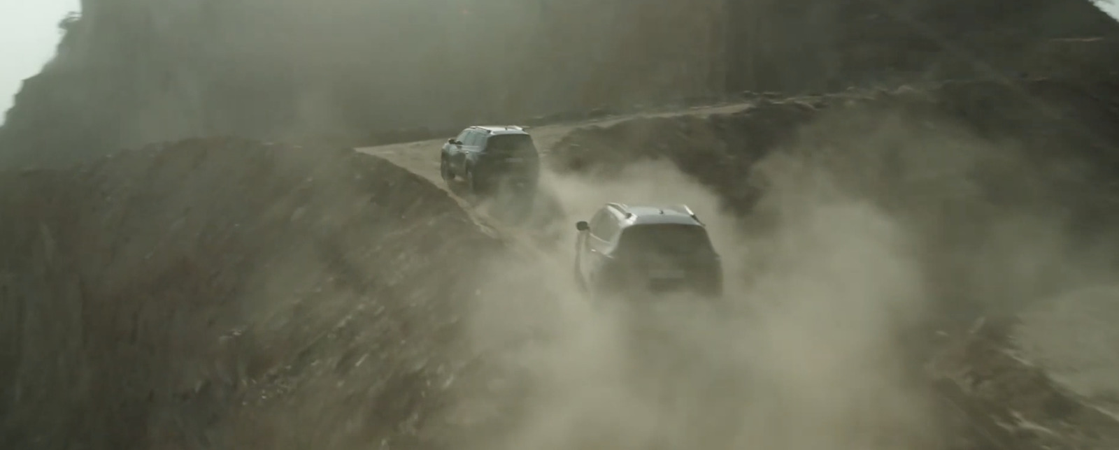 a couple of cars driving down a dirt road