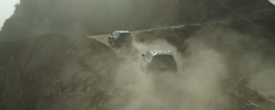 a couple of cars driving down a dirt road