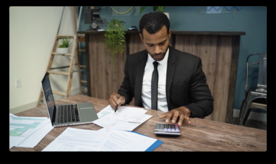 a man in a suit sitting at a table with a calculator and laptop