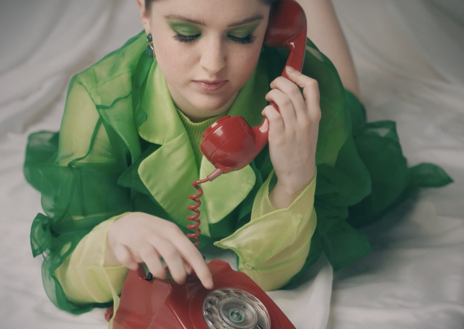 a woman laying on a bed talking on a red telephone