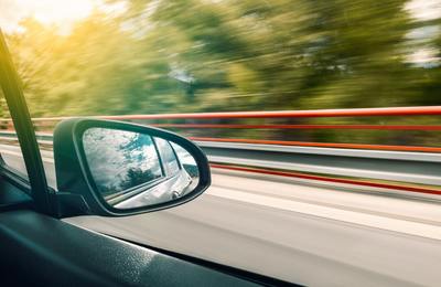 a car's side view mirror with trees in the background