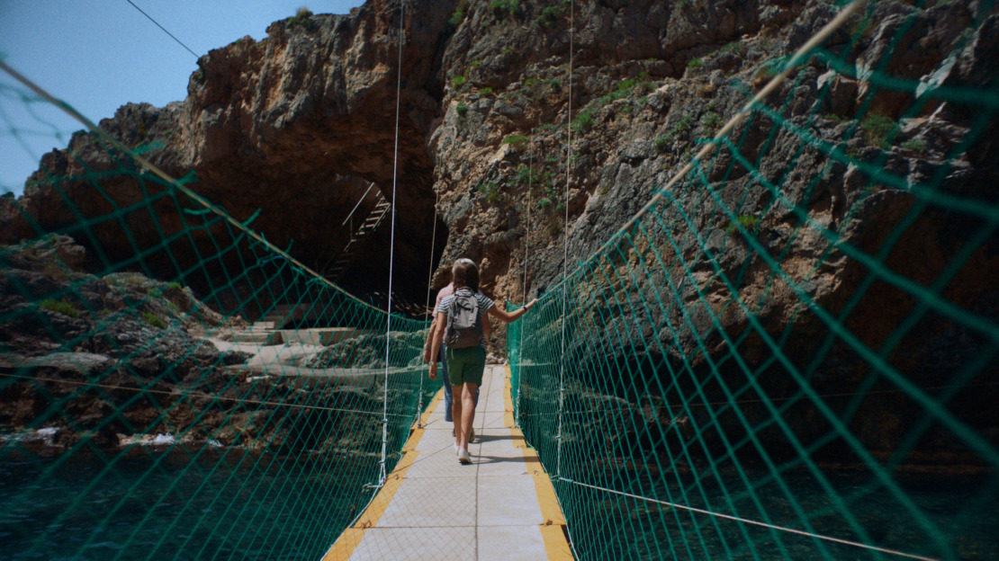 a woman walking across a suspension bridge over water