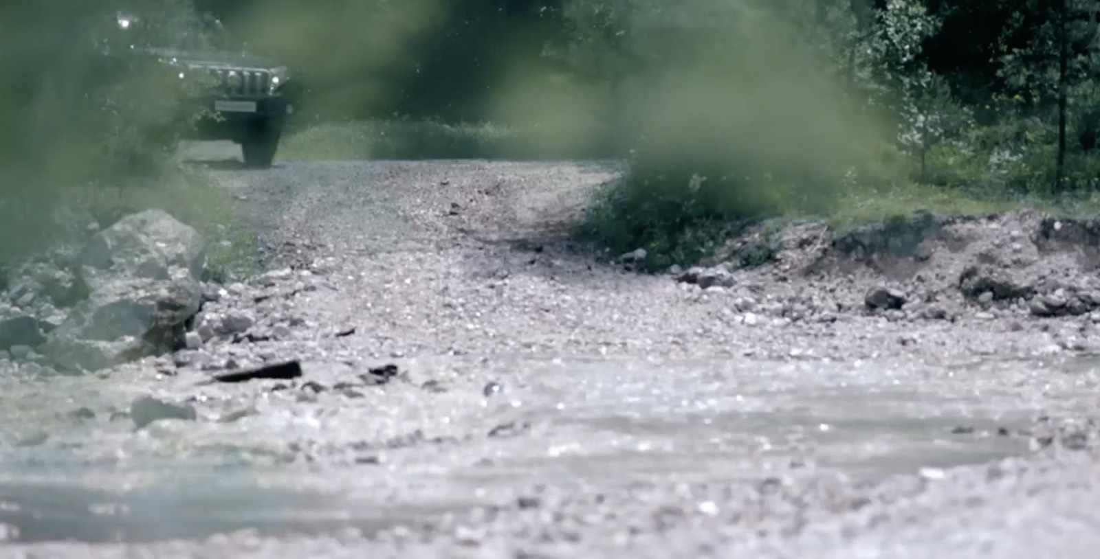 a truck driving down a dirt road next to a river