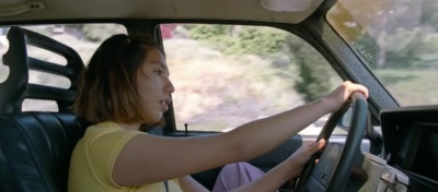 a woman sitting in a car with her hand on the steering wheel