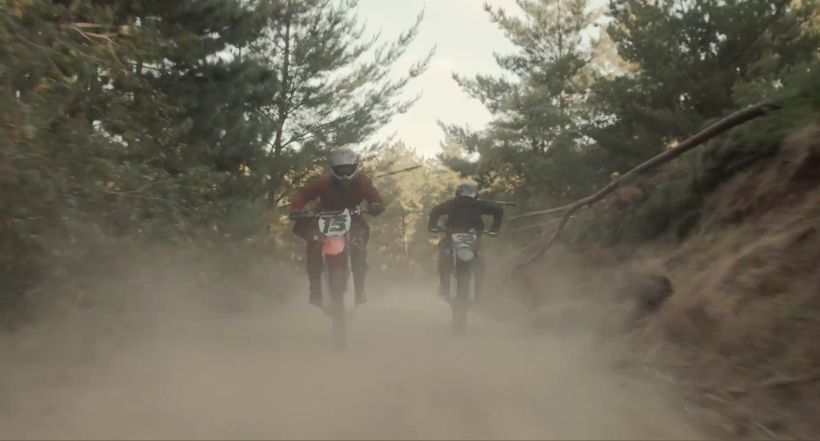 two people riding dirt bikes on a dirt road