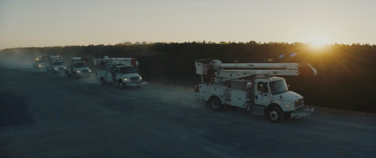 a group of trucks driving down a road next to a forest