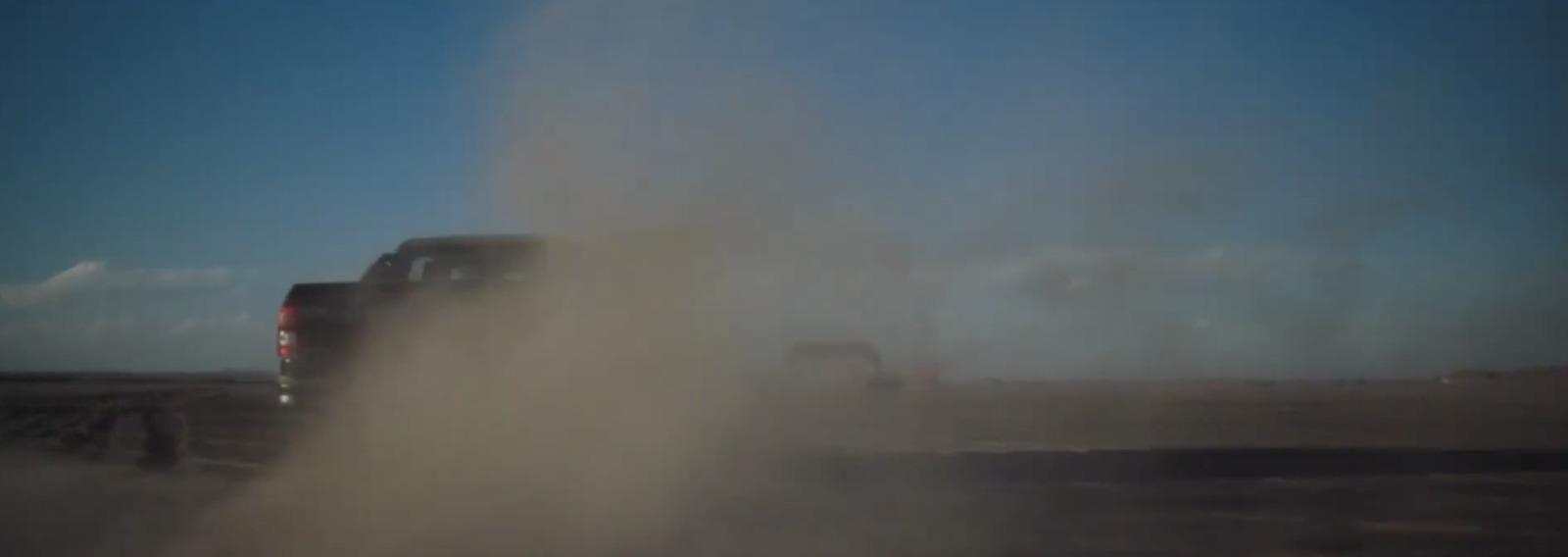 a truck driving down a road with a lot of dust