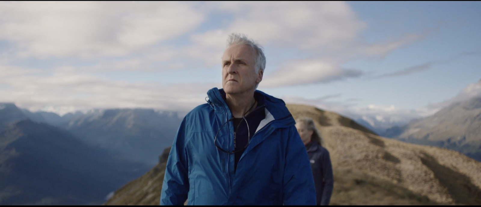 a man in a blue jacket standing on top of a mountain