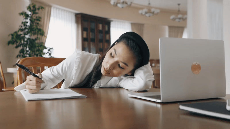 a woman sitting at a table writing on a piece of paper