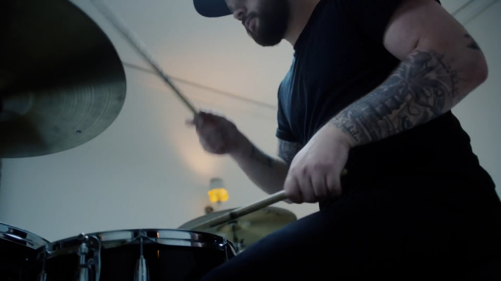 a man with tattoos playing drums in a room