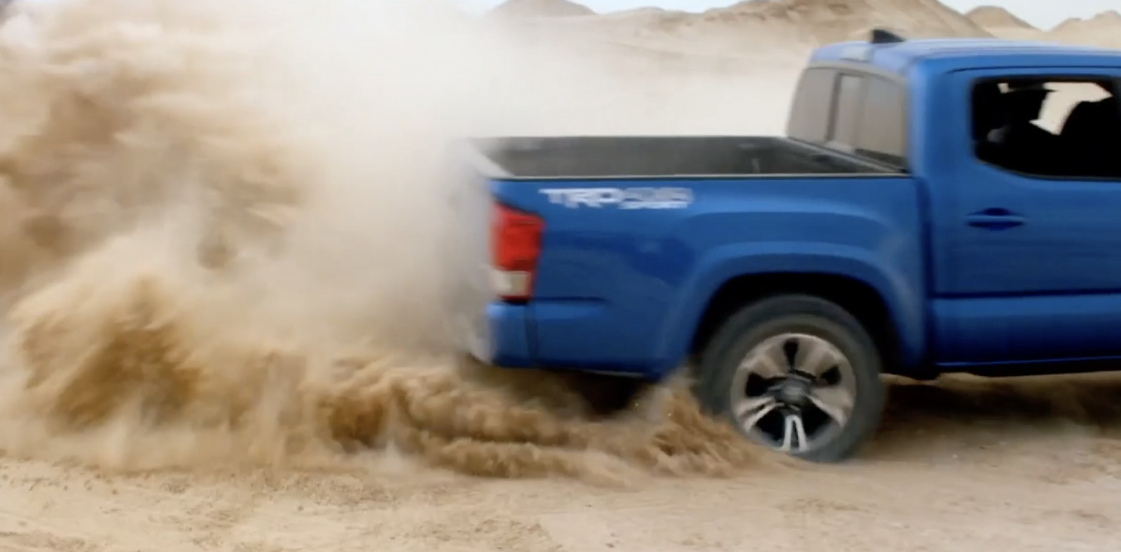 a blue pick up truck driving through sand