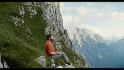 a man sitting on top of a mountain using a laptop computer