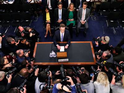 a man sitting at a table surrounded by photographers