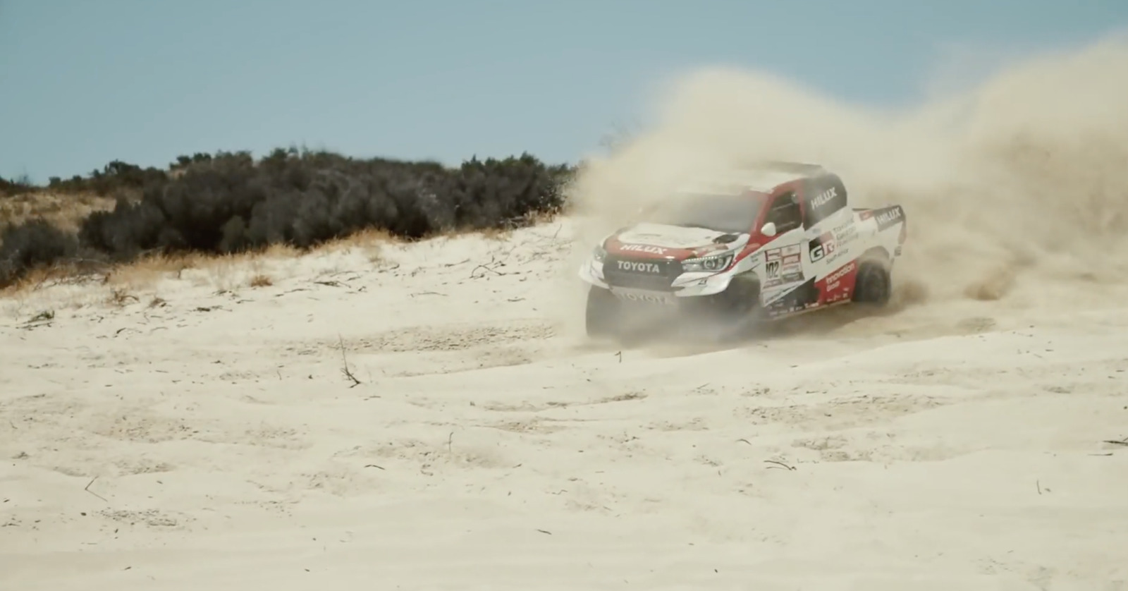 a truck driving through the sand on a sunny day