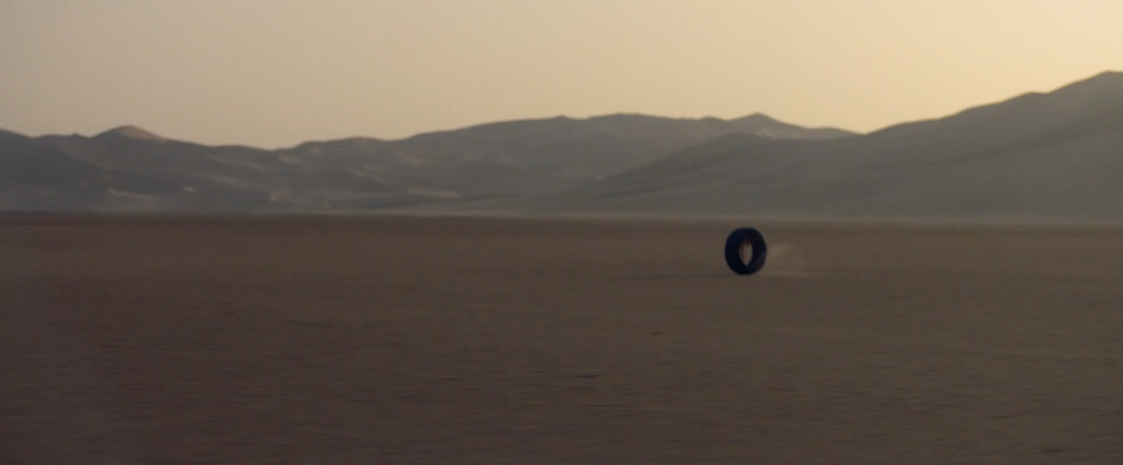 a tire in the middle of a desert with mountains in the background