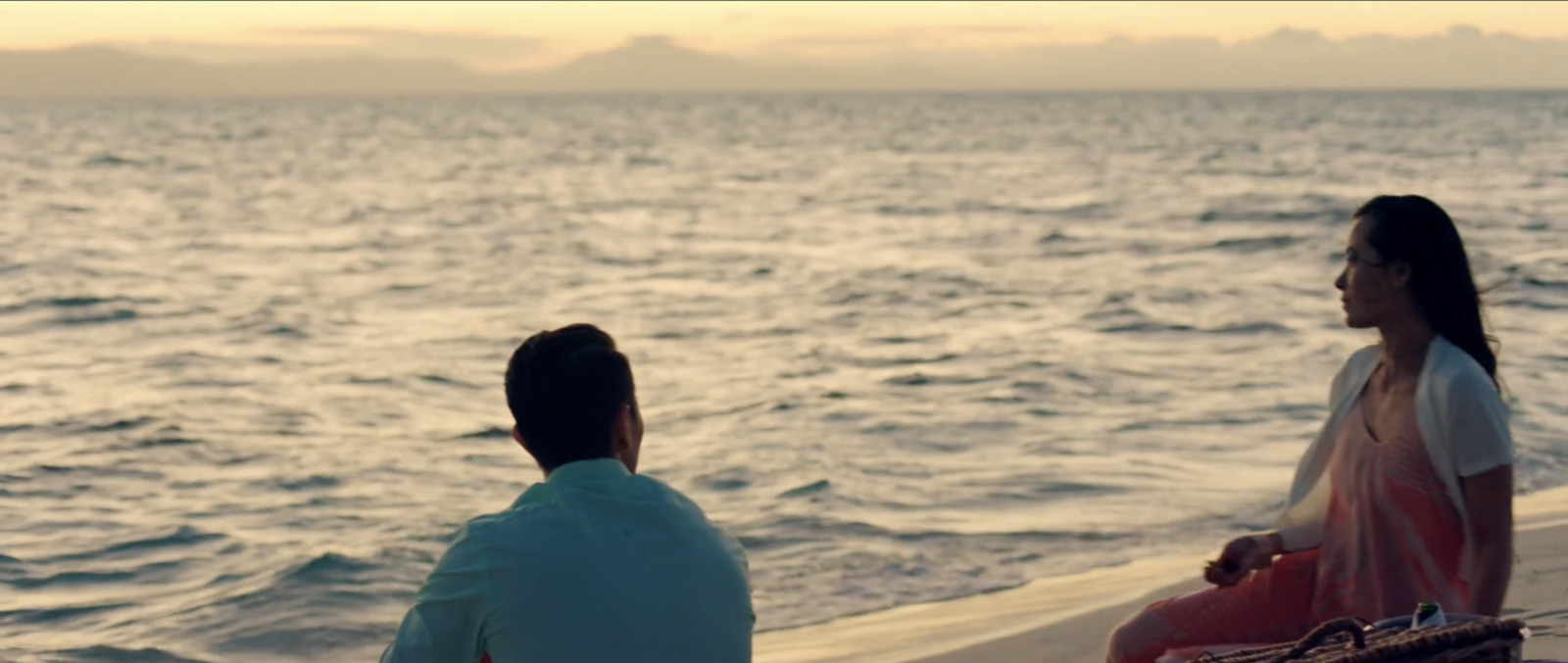 a man and a woman sitting on a beach next to the ocean