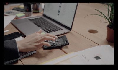 a person typing on a calculator in front of a laptop