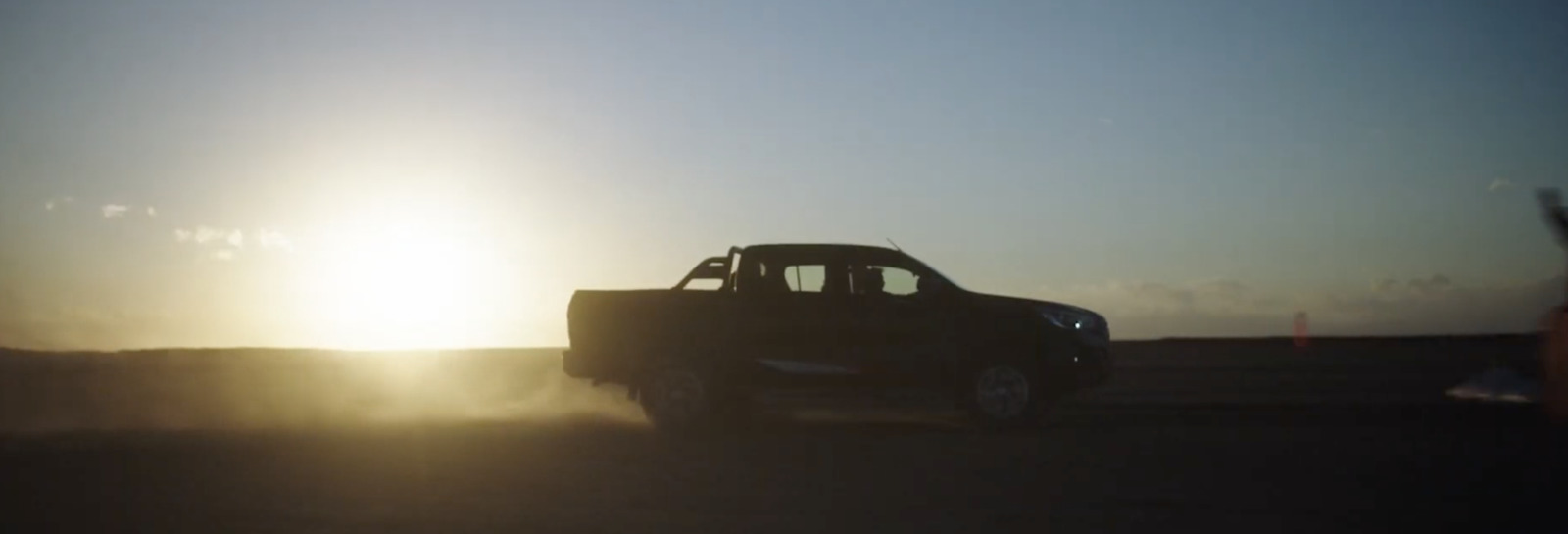 a truck driving down a road with the sun in the background