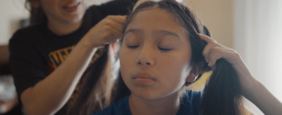 a young girl getting her hair styled by a woman