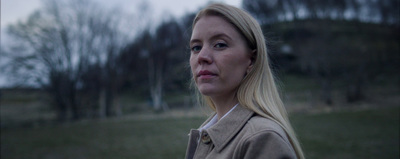 a woman standing in a field with trees in the background