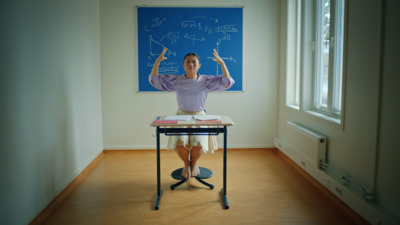 a woman sitting at a desk in front of a chalkboard