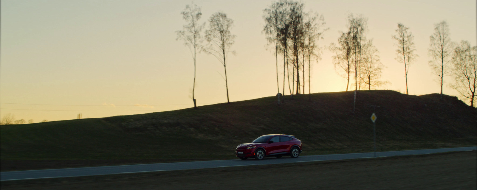 a red car driving down a road next to a hill