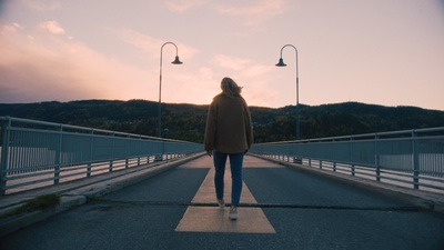 a woman walking across a bridge at sunset