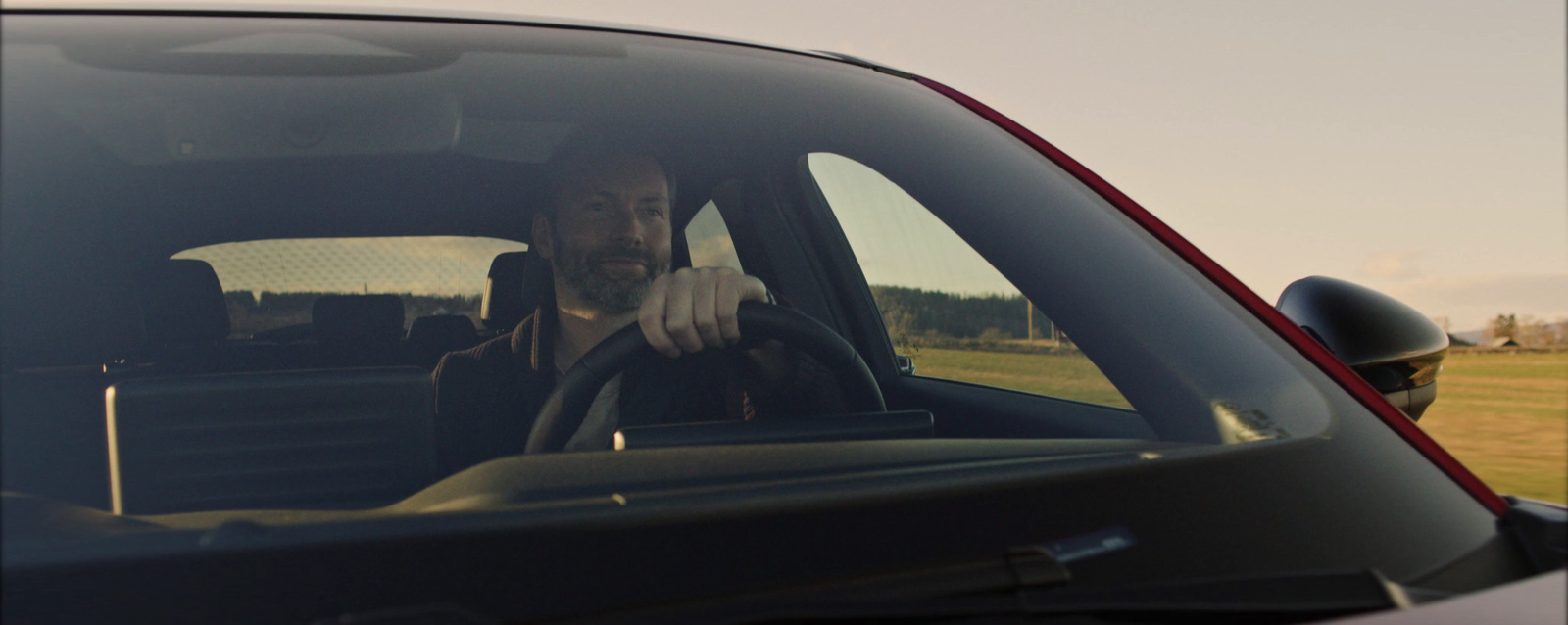 a man sitting in a car with his hand on the steering wheel