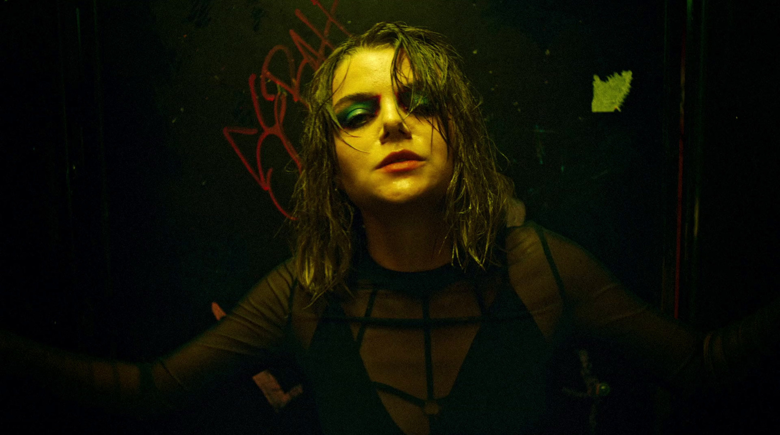 a woman with long hair and green eyes standing in a dark room