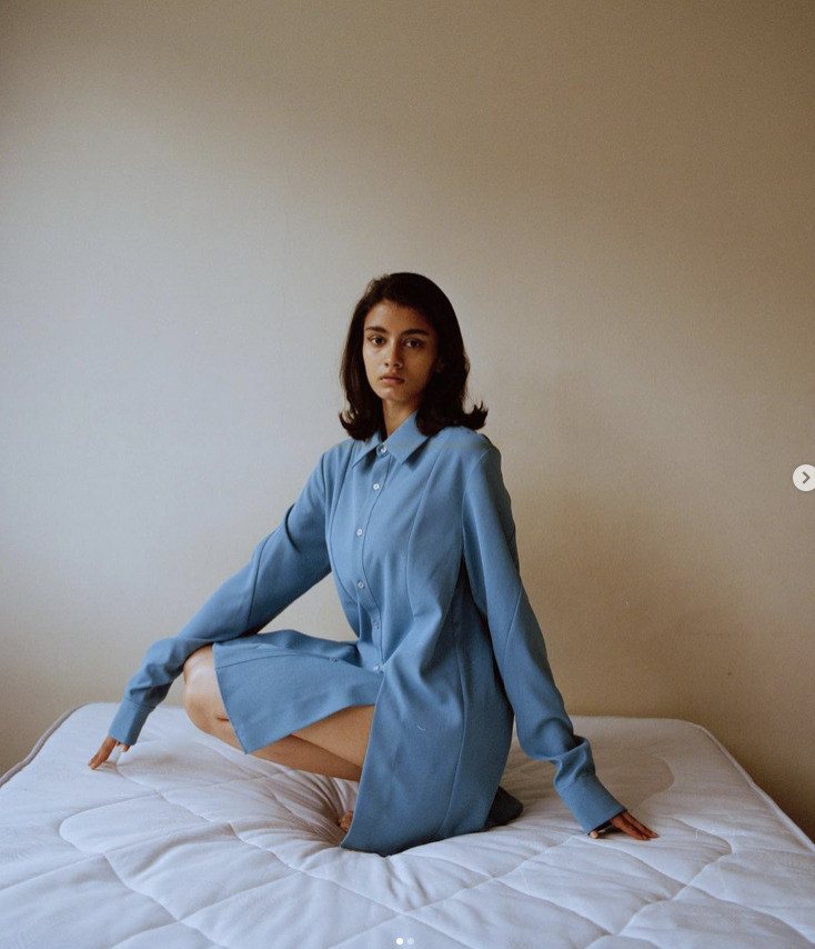 a woman sitting on a bed in a blue shirt dress