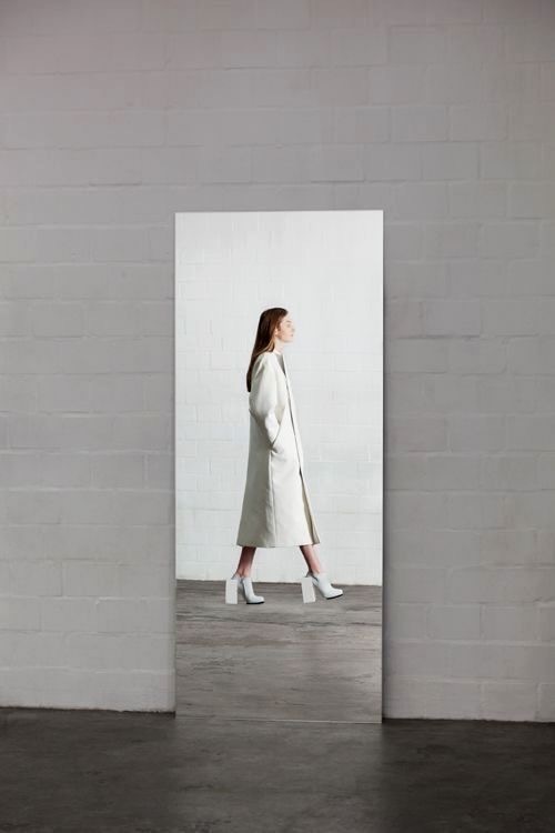 a woman in a white coat walking through a white room