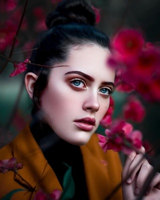 a woman with blue eyes standing in front of pink flowers