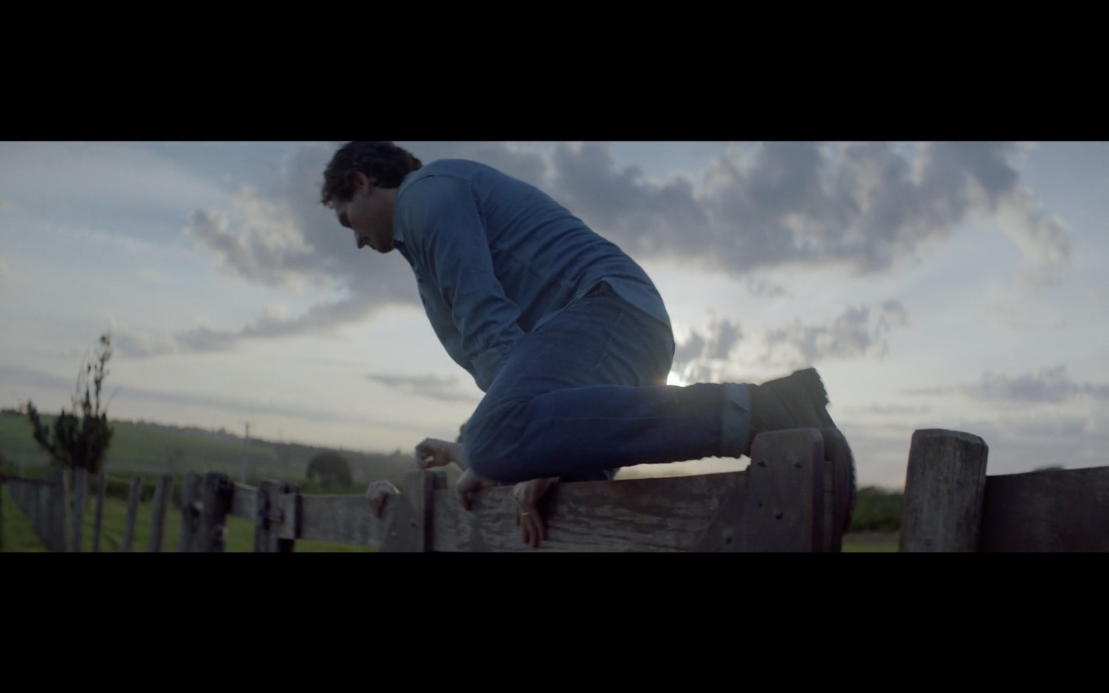 a man leaning on a wooden fence in a field