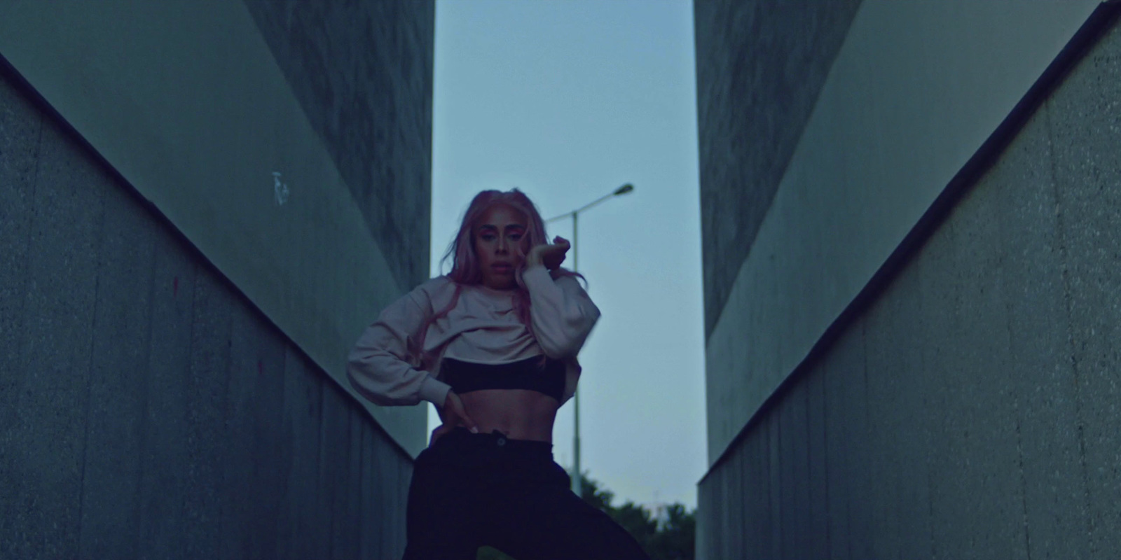 a woman in a black top and black pants is standing in an alleyway