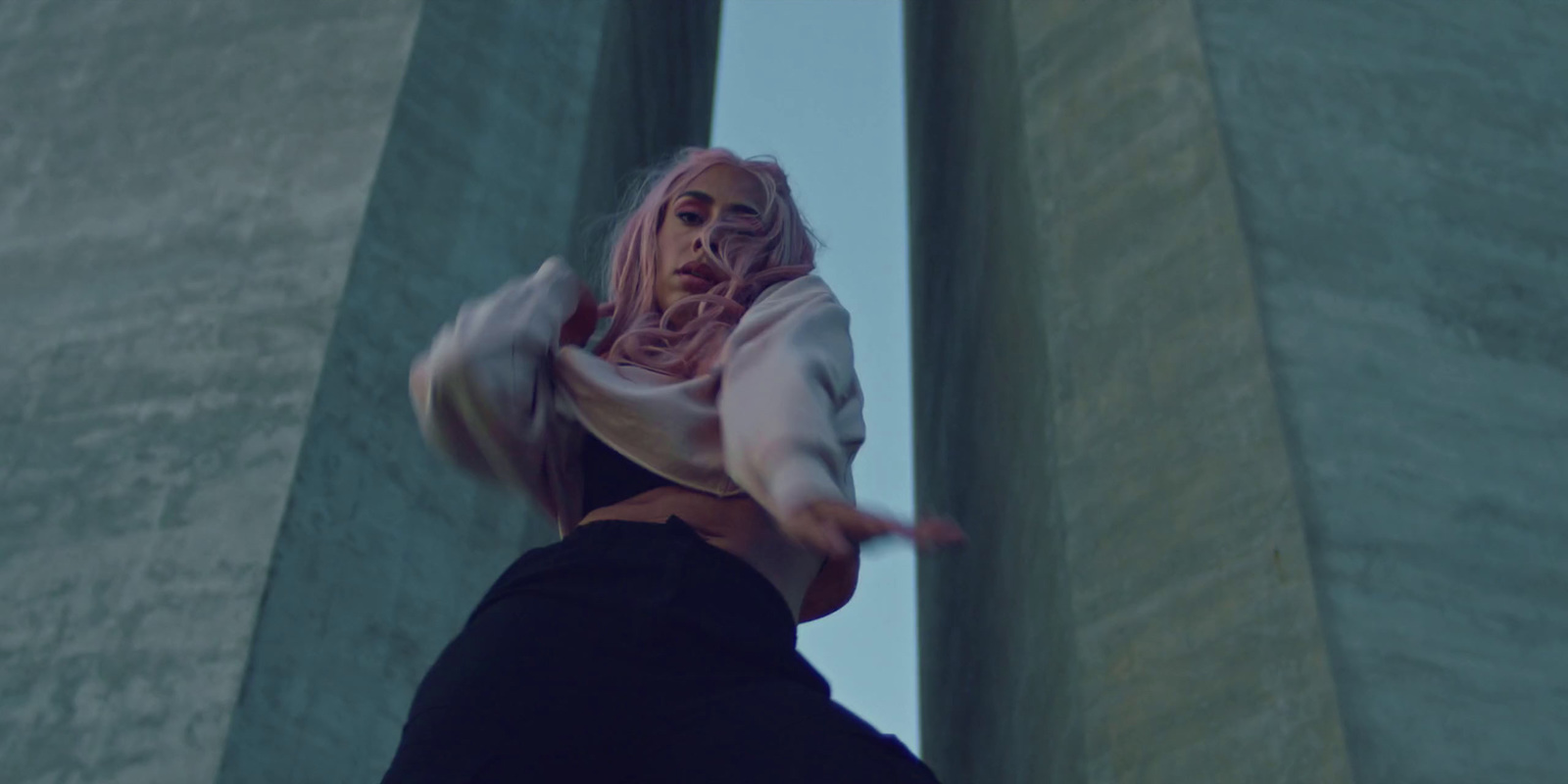 a woman with pink hair is dancing in front of pillars