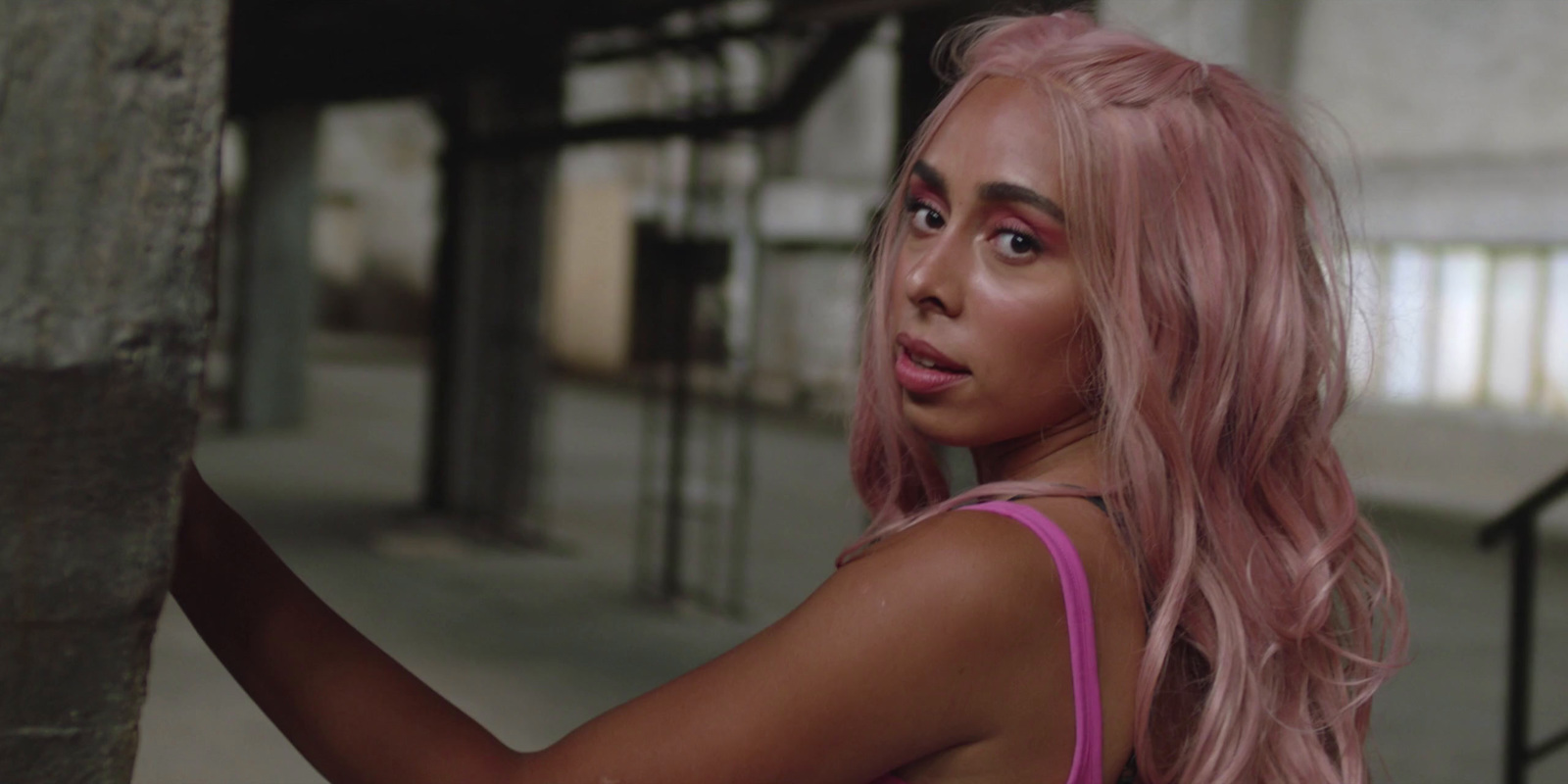 a woman with pink hair leaning against a wall