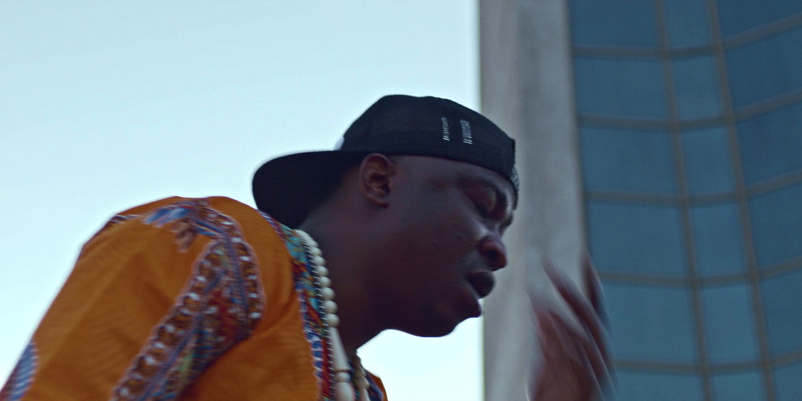 a man wearing a hat and necklace in front of a building