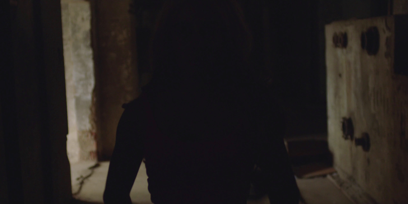 a woman is walking down a hallway in a dark room