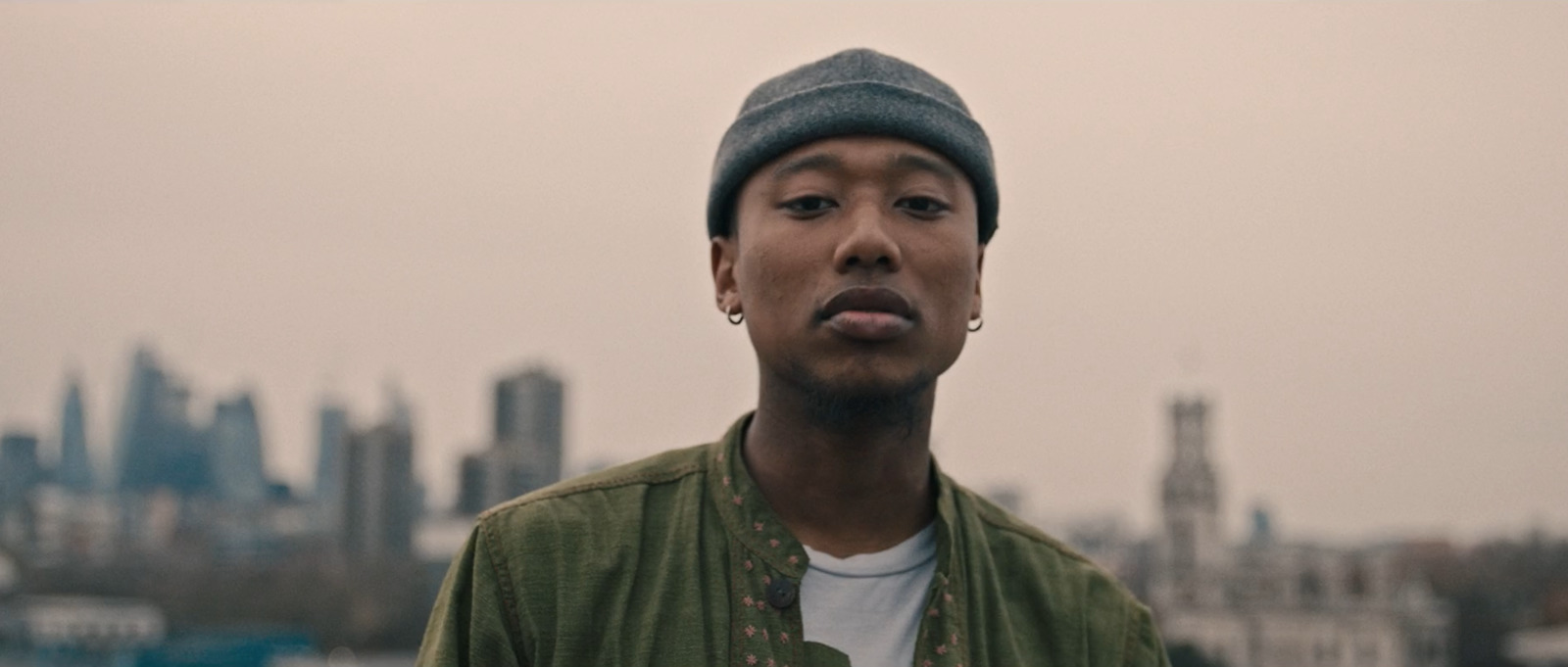 a man in a green jacket with a city in the background