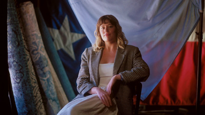 a woman sitting on a chair in front of a curtain