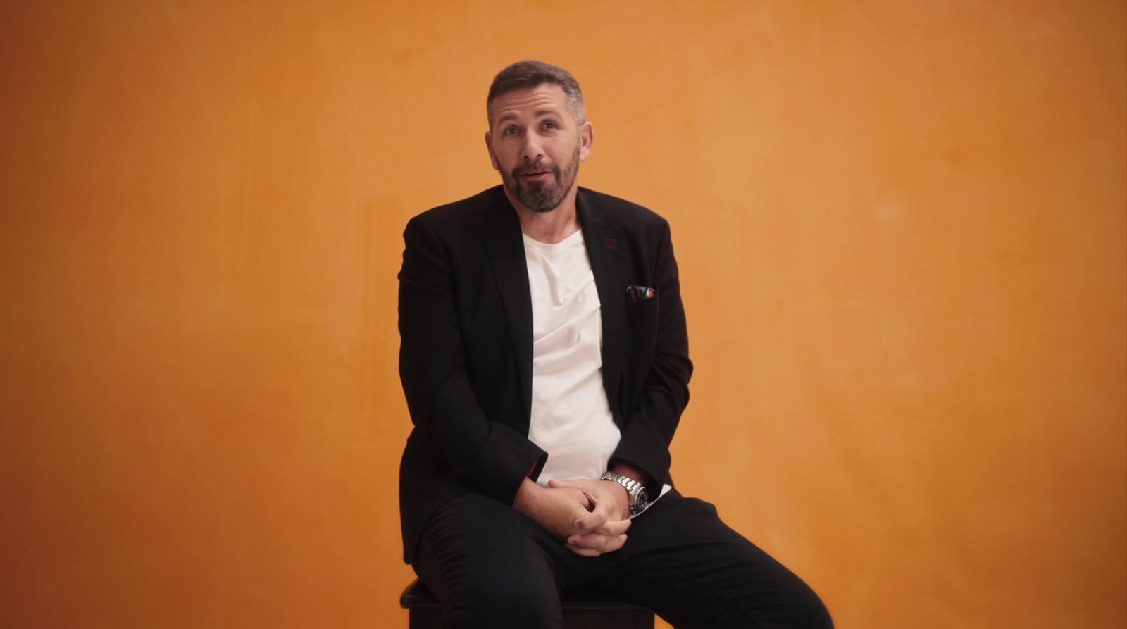 a man sitting on a stool in front of an orange wall