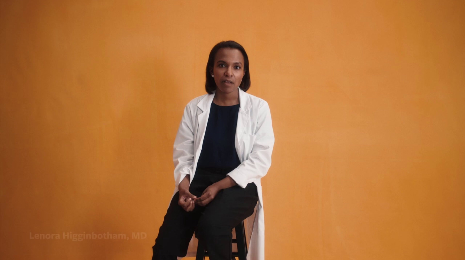 a woman sitting on a stool in front of an orange wall