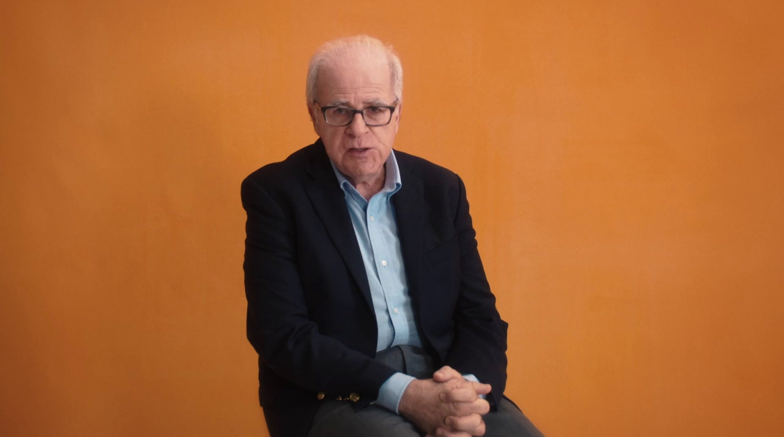 a man sitting on top of a chair in front of an orange wall