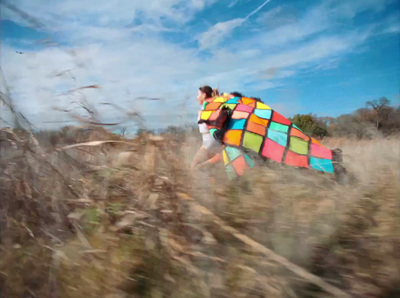 a woman carrying a colorful kite through a field