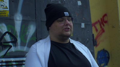 a man wearing a beanie and glasses standing in front of a wall