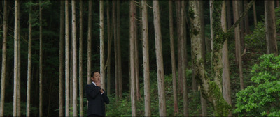 a man in a suit standing in front of a forest